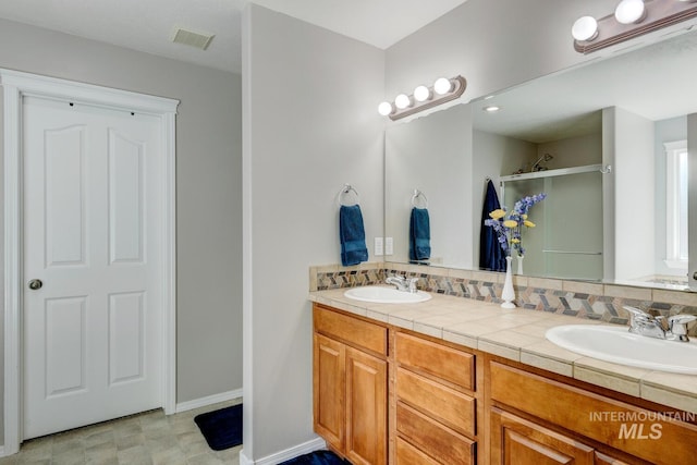 full bath featuring double vanity, visible vents, a stall shower, and a sink