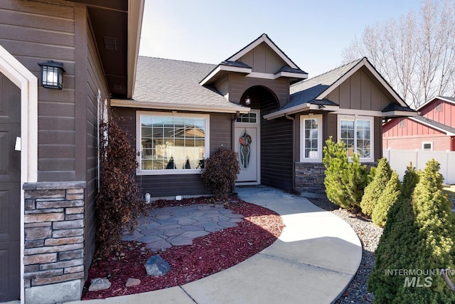 view of front facade with board and batten siding, fence, roof with shingles, a garage, and stone siding