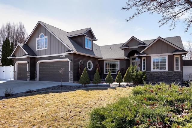 craftsman-style home featuring stone siding, fence, board and batten siding, concrete driveway, and an attached garage