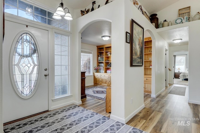 foyer with light wood finished floors, a notable chandelier, a healthy amount of sunlight, and arched walkways