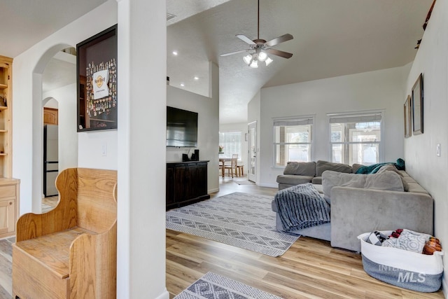 living area with a ceiling fan, light wood-style floors, arched walkways, and high vaulted ceiling