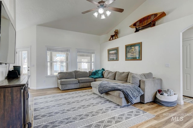 living room featuring baseboards, ceiling fan, light wood-type flooring, vaulted ceiling, and arched walkways