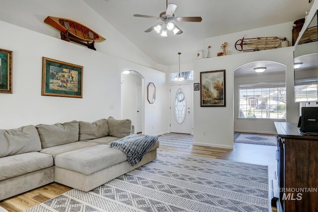 living area featuring baseboards, light wood-type flooring, vaulted ceiling, arched walkways, and a ceiling fan