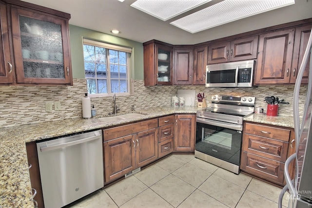 kitchen with appliances with stainless steel finishes, sink, light stone counters, and backsplash