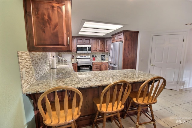 kitchen featuring light stone counters, stainless steel appliances, light tile patterned floors, decorative backsplash, and kitchen peninsula