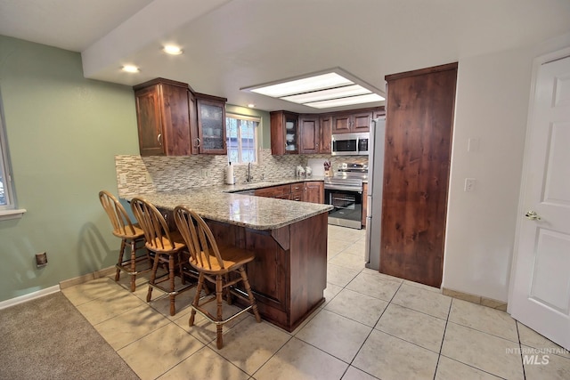 kitchen featuring stainless steel appliances, a kitchen bar, light tile patterned floors, sink, and kitchen peninsula