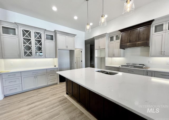 kitchen with light wood-type flooring, premium range hood, gray cabinetry, stainless steel gas cooktop, and hanging light fixtures