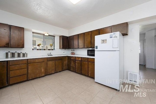 kitchen with black microwave, light countertops, freestanding refrigerator, visible vents, and a sink
