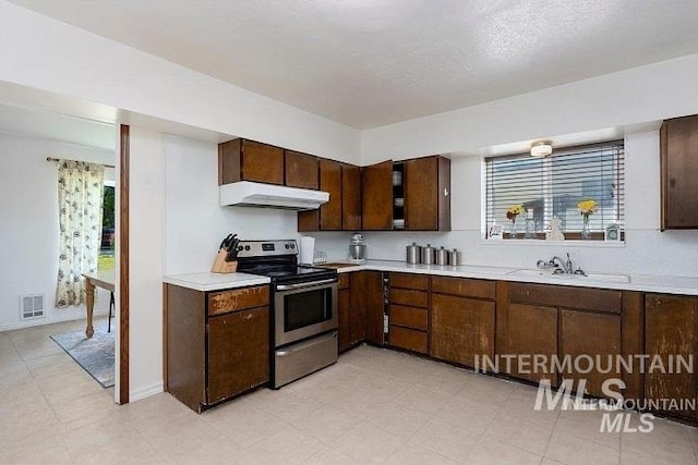 kitchen with under cabinet range hood, light countertops, a wealth of natural light, and electric stove