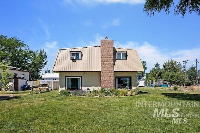 rear view of house with metal roof, a chimney, fence, and a lawn