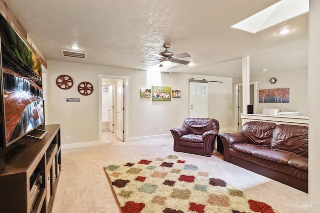 carpeted living room with ceiling fan, a textured ceiling, a skylight, and a barn door