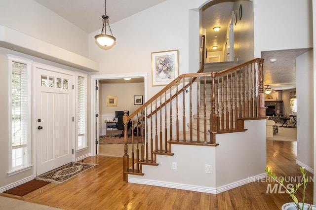 foyer featuring high vaulted ceiling, a fireplace, wood finished floors, baseboards, and stairs