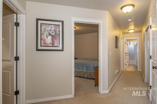 hallway with light carpet, a textured ceiling, and baseboards