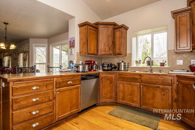 kitchen with light wood finished floors, an inviting chandelier, a sink, dishwasher, and a peninsula