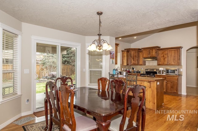 dining area featuring vaulted ceiling, a textured ceiling, a chandelier, light wood-type flooring, and baseboards