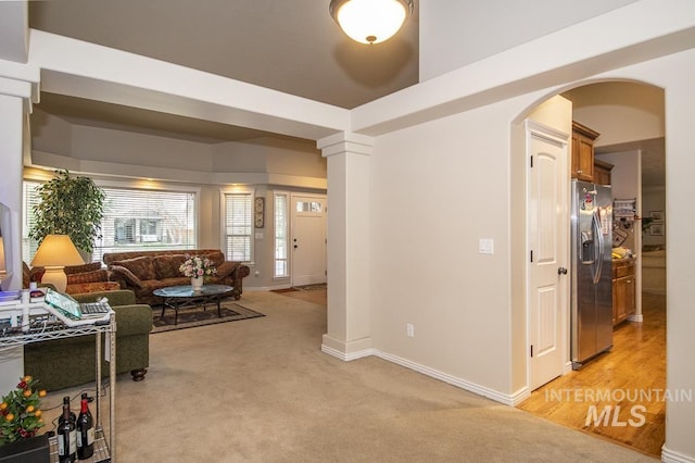 living area featuring arched walkways, light colored carpet, decorative columns, and baseboards