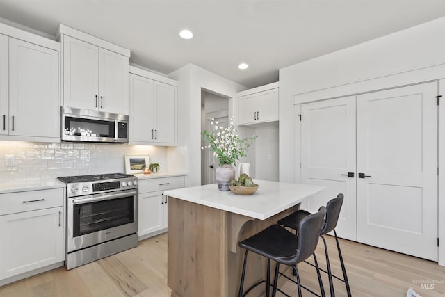 kitchen with tasteful backsplash, white cabinets, stainless steel appliances, light countertops, and light wood-style floors