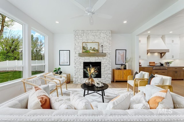 living room featuring a stone fireplace, ceiling fan, and light hardwood / wood-style flooring