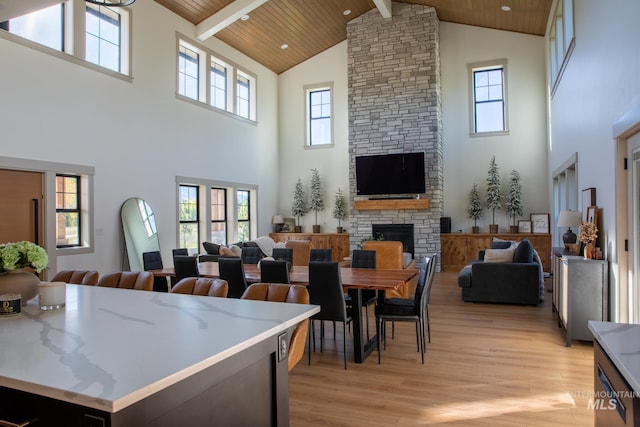 dining room with a stone fireplace, beam ceiling, wooden ceiling, light wood-type flooring, and high vaulted ceiling