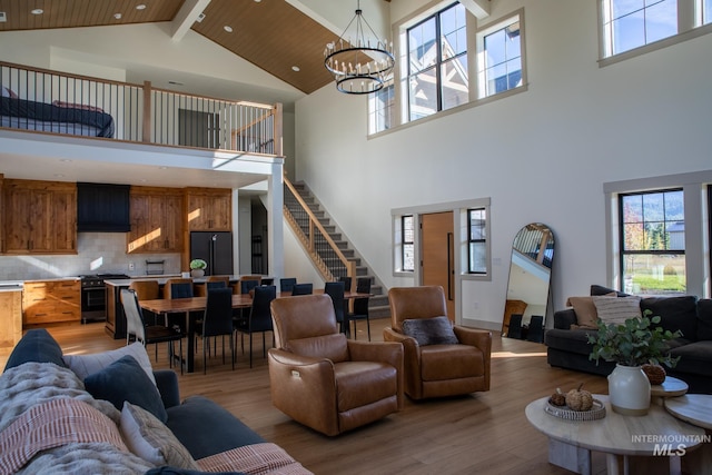 living room featuring light hardwood / wood-style floors, an inviting chandelier, beam ceiling, and high vaulted ceiling