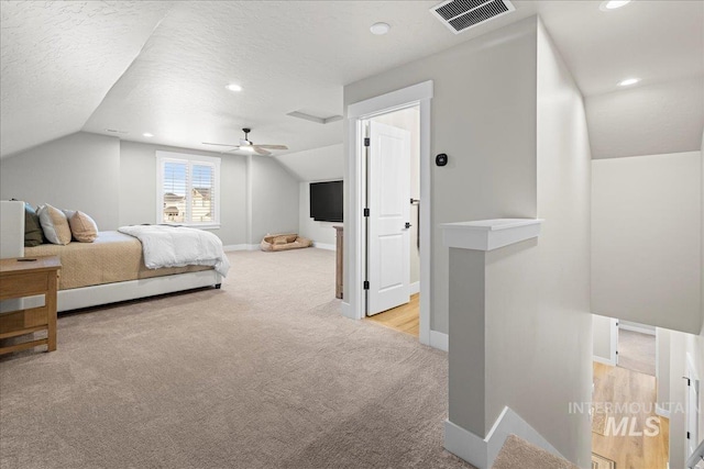 bedroom featuring ceiling fan, vaulted ceiling, light carpet, and a textured ceiling