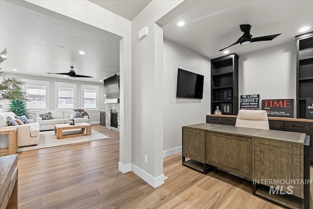 office space featuring ceiling fan, built in shelves, light wood-type flooring, and a fireplace