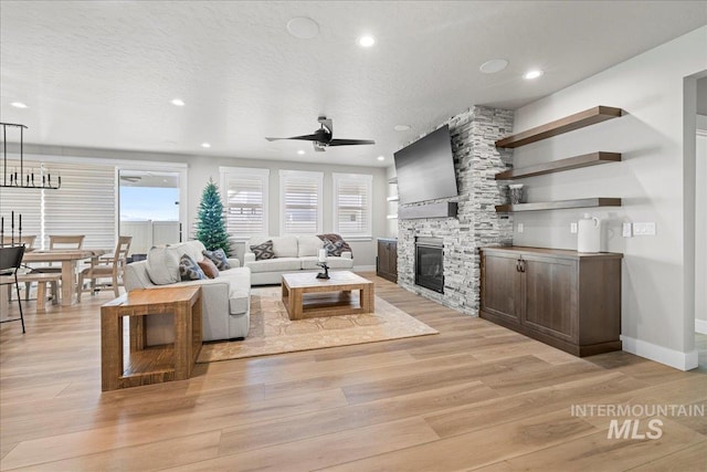 living room featuring light wood-type flooring, ceiling fan, a wealth of natural light, and a stone fireplace