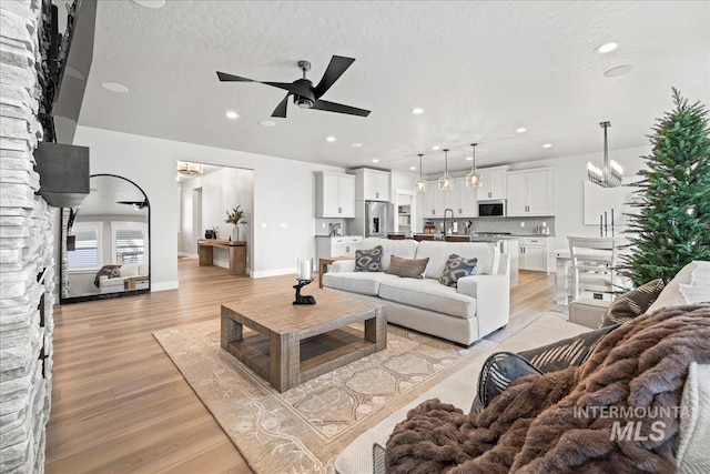 living room featuring ceiling fan with notable chandelier, light hardwood / wood-style floors, and a textured ceiling