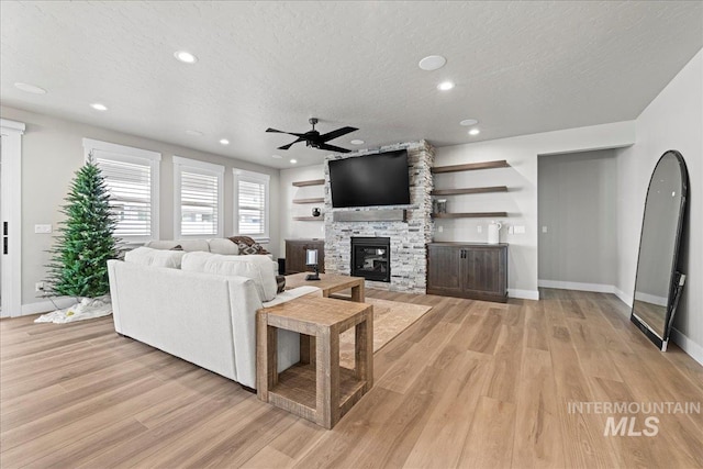 living room with ceiling fan, light wood-type flooring, a fireplace, and a textured ceiling