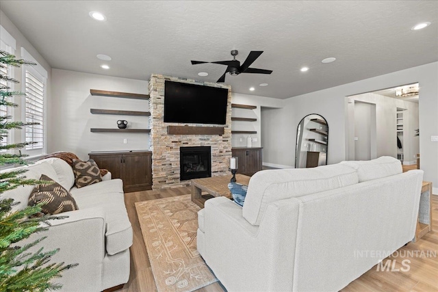 living room featuring ceiling fan, a textured ceiling, light wood-type flooring, and a fireplace