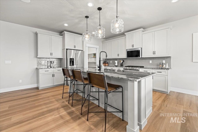 kitchen with tasteful backsplash, a center island with sink, a kitchen bar, white cabinetry, and stainless steel appliances