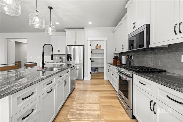 kitchen with appliances with stainless steel finishes, tasteful backsplash, hanging light fixtures, white cabinets, and sink