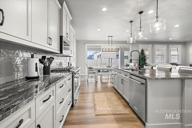 kitchen with pendant lighting, white cabinetry, appliances with stainless steel finishes, and a kitchen island with sink