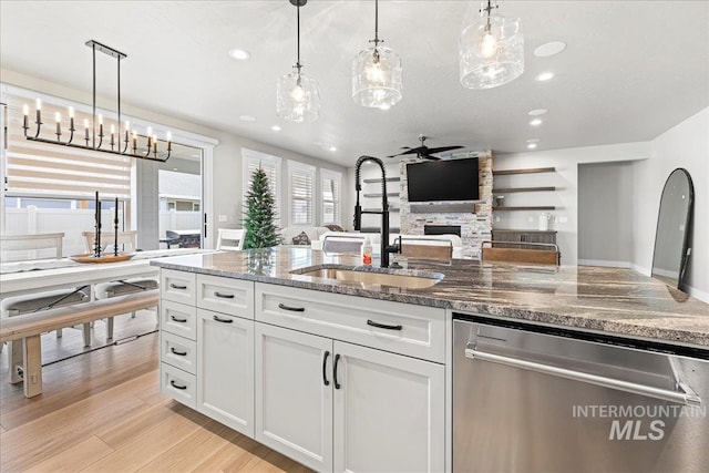 kitchen with decorative light fixtures, a fireplace, dishwasher, white cabinets, and sink