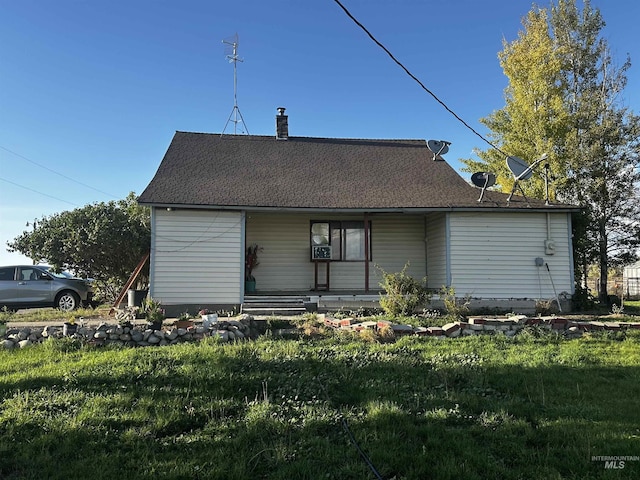 back of house featuring a shingled roof, a lawn, and a chimney