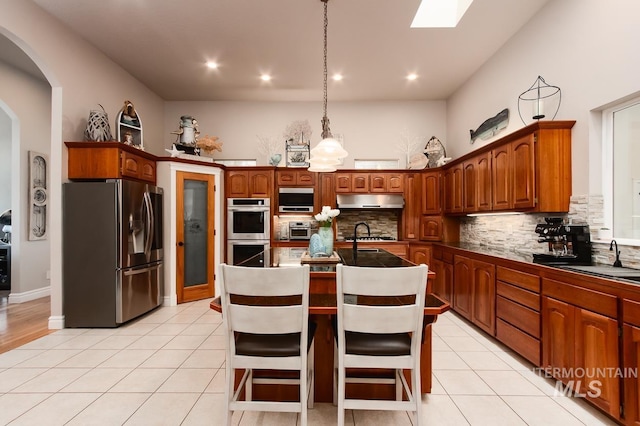 kitchen featuring light tile patterned floors, stainless steel appliances, tasteful backsplash, a sink, and under cabinet range hood