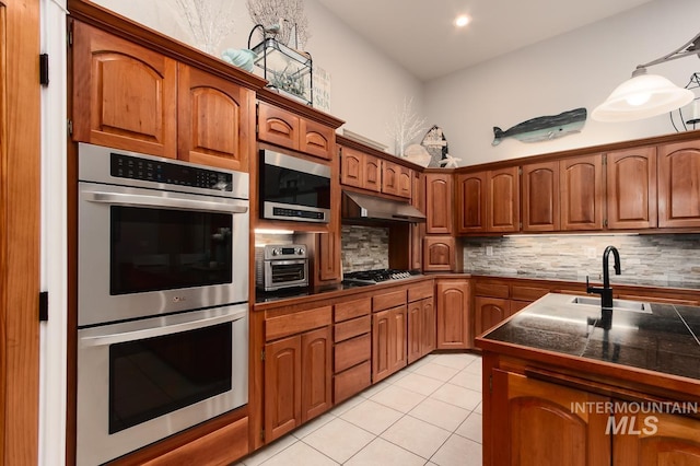 kitchen with brown cabinets, appliances with stainless steel finishes, a sink, and under cabinet range hood