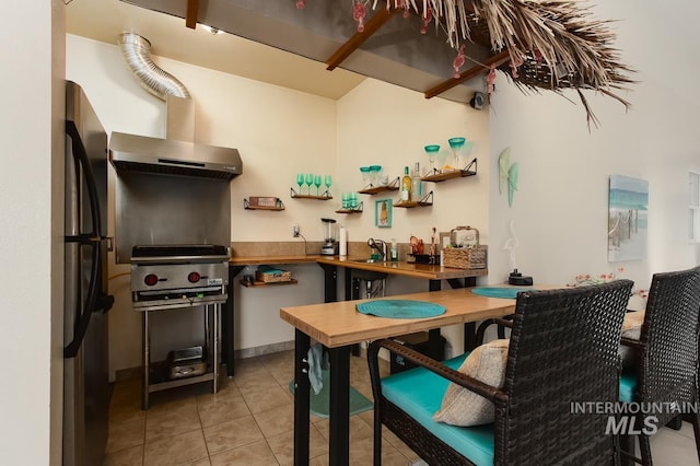 kitchen featuring freestanding refrigerator, a sink, wall chimney range hood, and light tile patterned floors