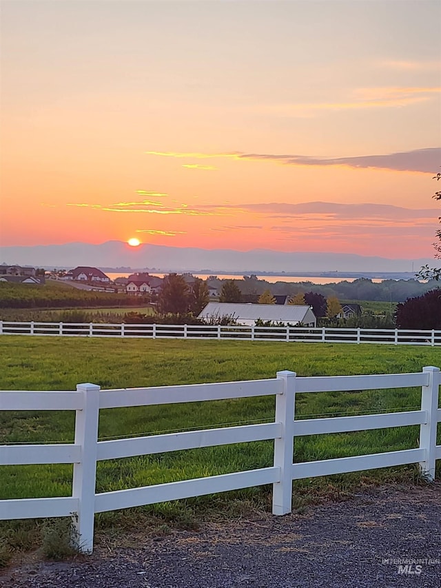 yard at dusk featuring fence, a mountain view, and a rural view