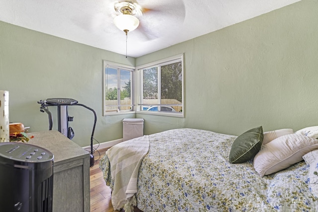 bedroom with ceiling fan, a textured wall, wood finished floors, and baseboards