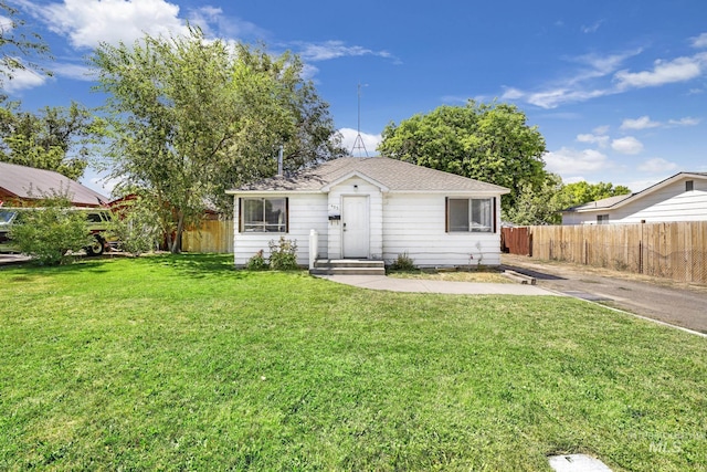 view of front of house with a shingled roof, a front yard, and fence