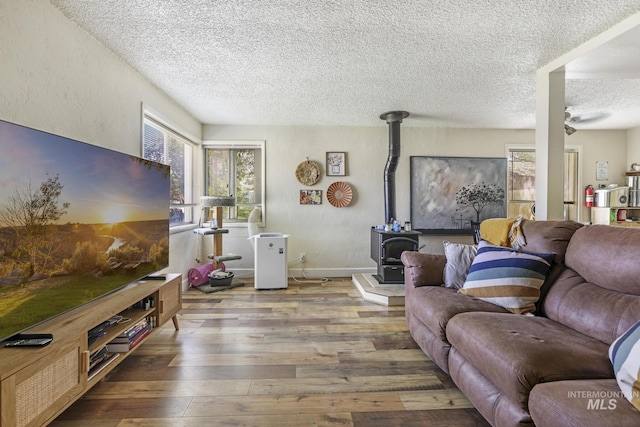 living room with a wood stove, a textured ceiling, baseboards, and hardwood / wood-style flooring