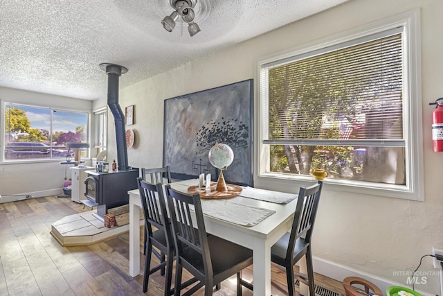 dining area with a textured wall, a wood stove, a textured ceiling, wood finished floors, and baseboards