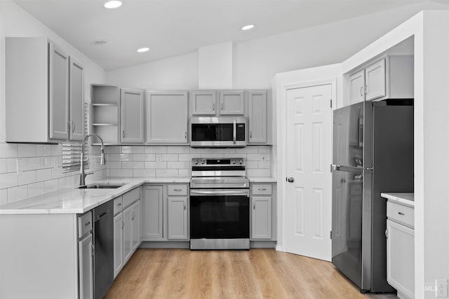 kitchen featuring gray cabinetry, light wood-style flooring, a sink, open shelves, and appliances with stainless steel finishes