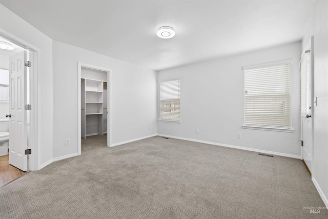 unfurnished bedroom with a spacious closet, visible vents, baseboards, and carpet floors