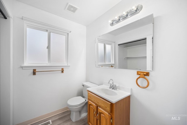 bathroom with toilet, wood finished floors, vanity, visible vents, and baseboards