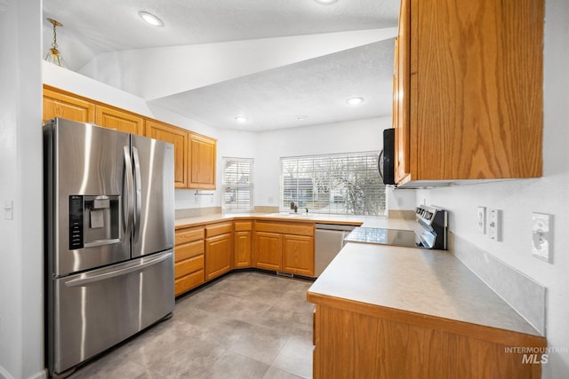 kitchen with stainless steel appliances, lofted ceiling, light countertops, brown cabinetry, and a sink