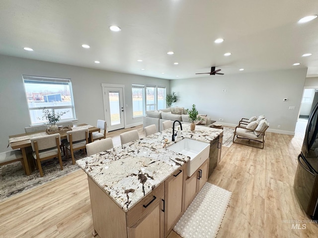 kitchen featuring light hardwood / wood-style floors, sink, light stone countertops, and an island with sink