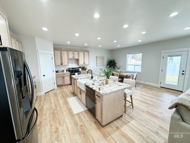 kitchen with sink, appliances with stainless steel finishes, an island with sink, a kitchen bar, and light brown cabinetry