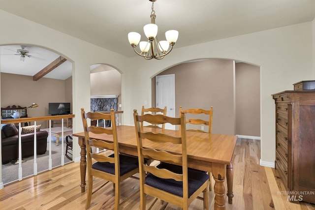 dining area featuring arched walkways, ceiling fan with notable chandelier, baseboards, and light wood-style floors